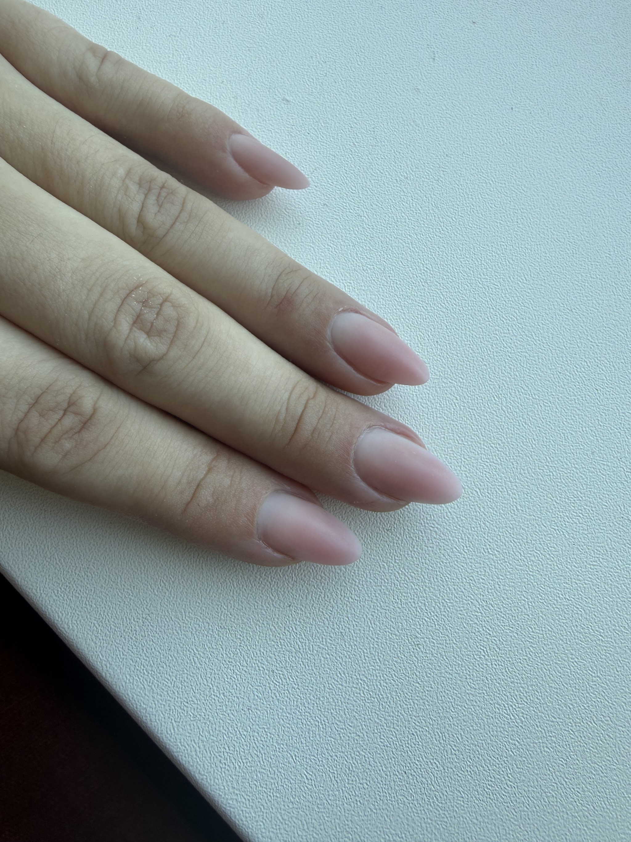 Lange nude amandelnagels op een wit bureau
