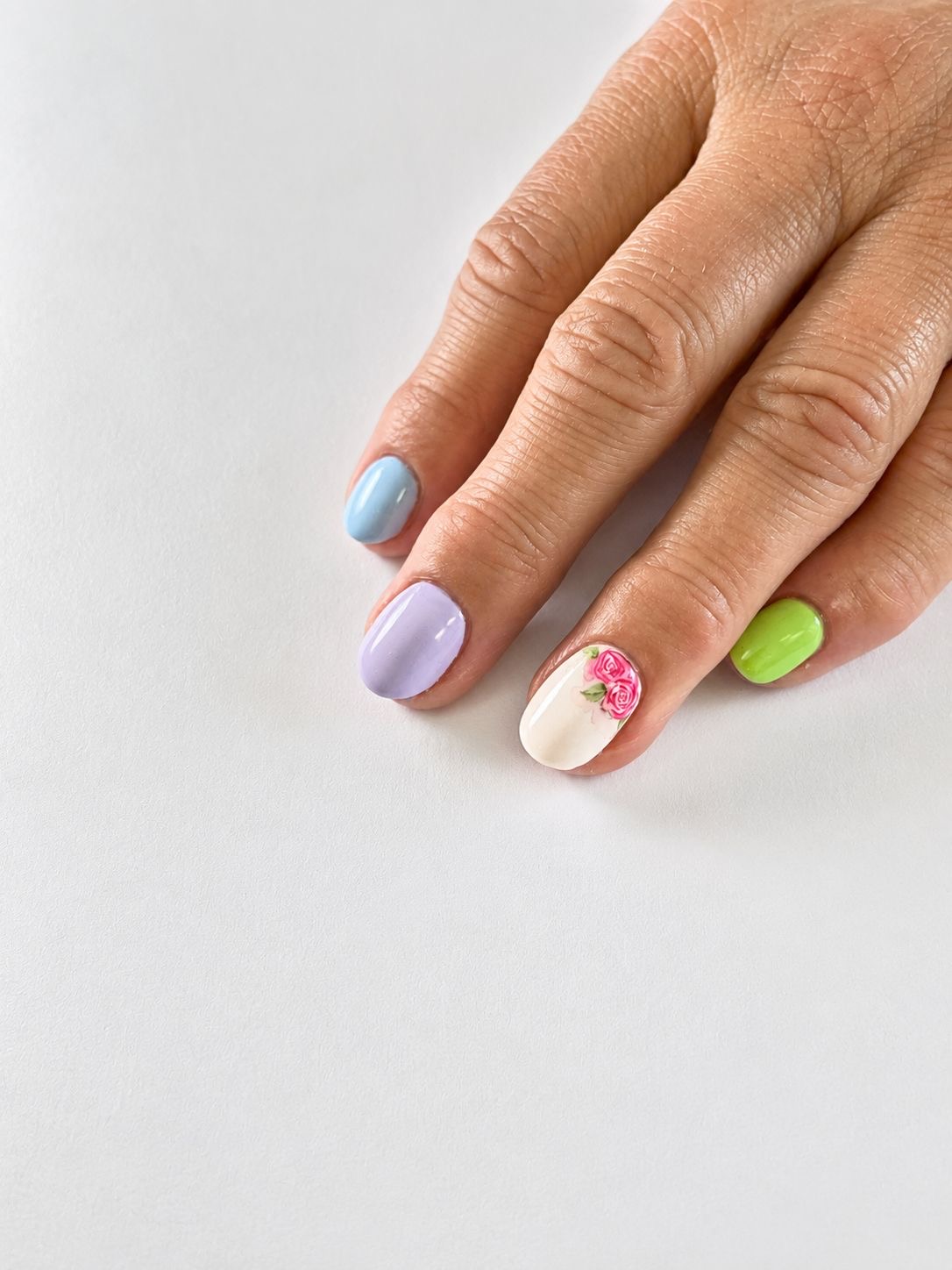 Korte nagels in pastelblauw, lila en limoengroen met een handgeschilderde bloem
